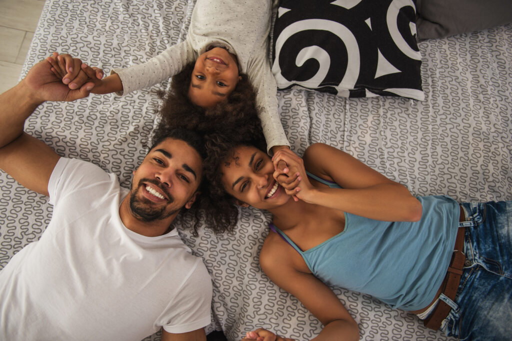 Photo illustrative de deux adultes et d’un enfant souriants, allongés et se tenant les mains.