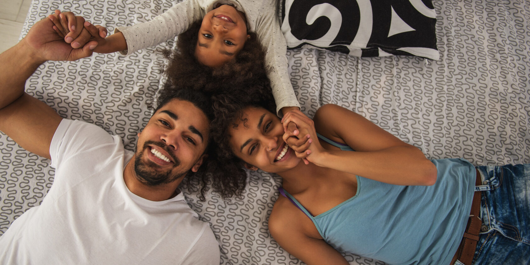 Assurance emprunteur : comprendre la carence et la franchise Photo illustrative de deux adultes et d’un enfant souriants, allongés et se tenant les mains.