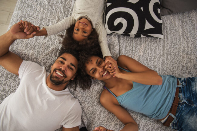 Photo illustrative de deux adultes et d’un enfant souriants, allongés et se tenant les mains.