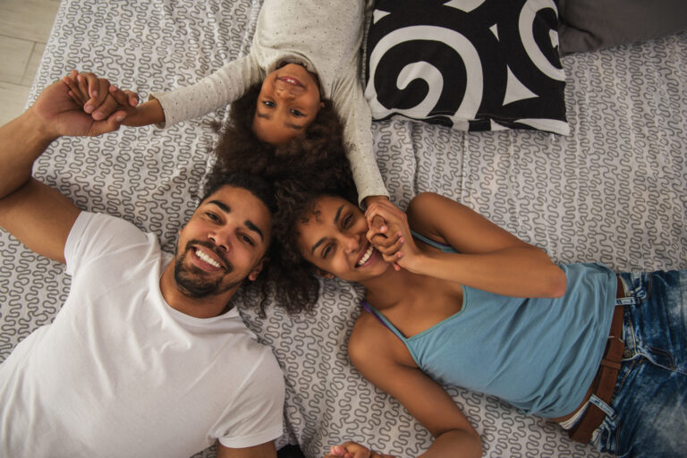 Photo illustrative de deux adultes et d’un enfant souriants, allongés et se tenant les mains.